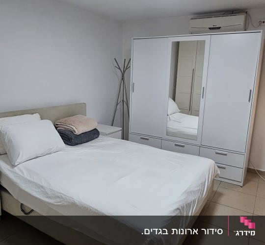 חדר שינה עם מיטה מסודרת וארון בגדים לבן
